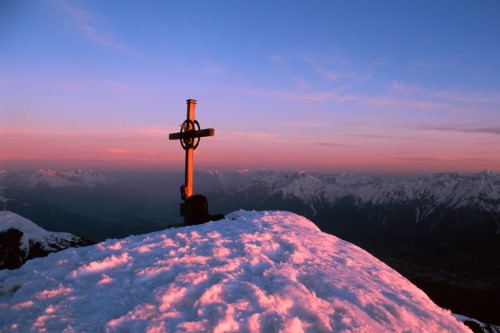 Alpengipfel mit Gipfelkreuz im Winter bei Sonnenuntergang