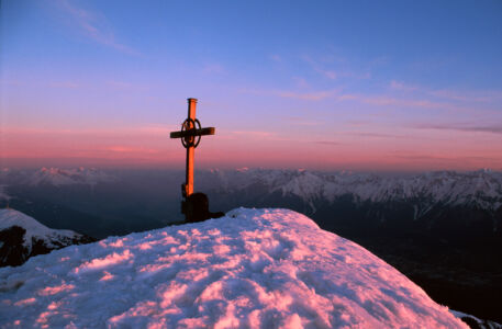 Alpengipfel mit Gipfelkreuz im Winter bei Sonnenuntergang